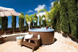 Un jacuzzi rodeado de árboles bien cuidados y un cielo azul despejado.