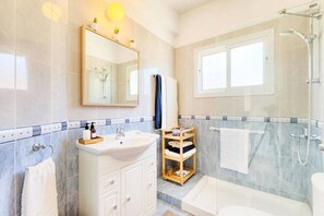 A modern bathroom with a white sink, mirror, and a glass-enclosed shower area.
