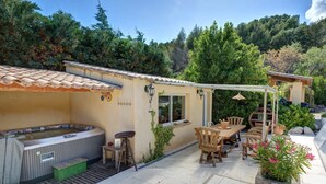 A patio with a hot tub, wooden furniture, and potted plants. - Les Gargoulettes (Lauris)