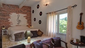A cozy room with a bed, a table, chairs, a guitar, and a brick wall with a treble clef and vinyl records. - Les Gargoulettes (Lauris)