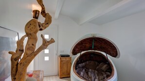 A room with a unique tree-shaped light fixture, a large round bed with a fur-lined interior, and a wooden cabinet. - Les Gargoulettes (Lauris)