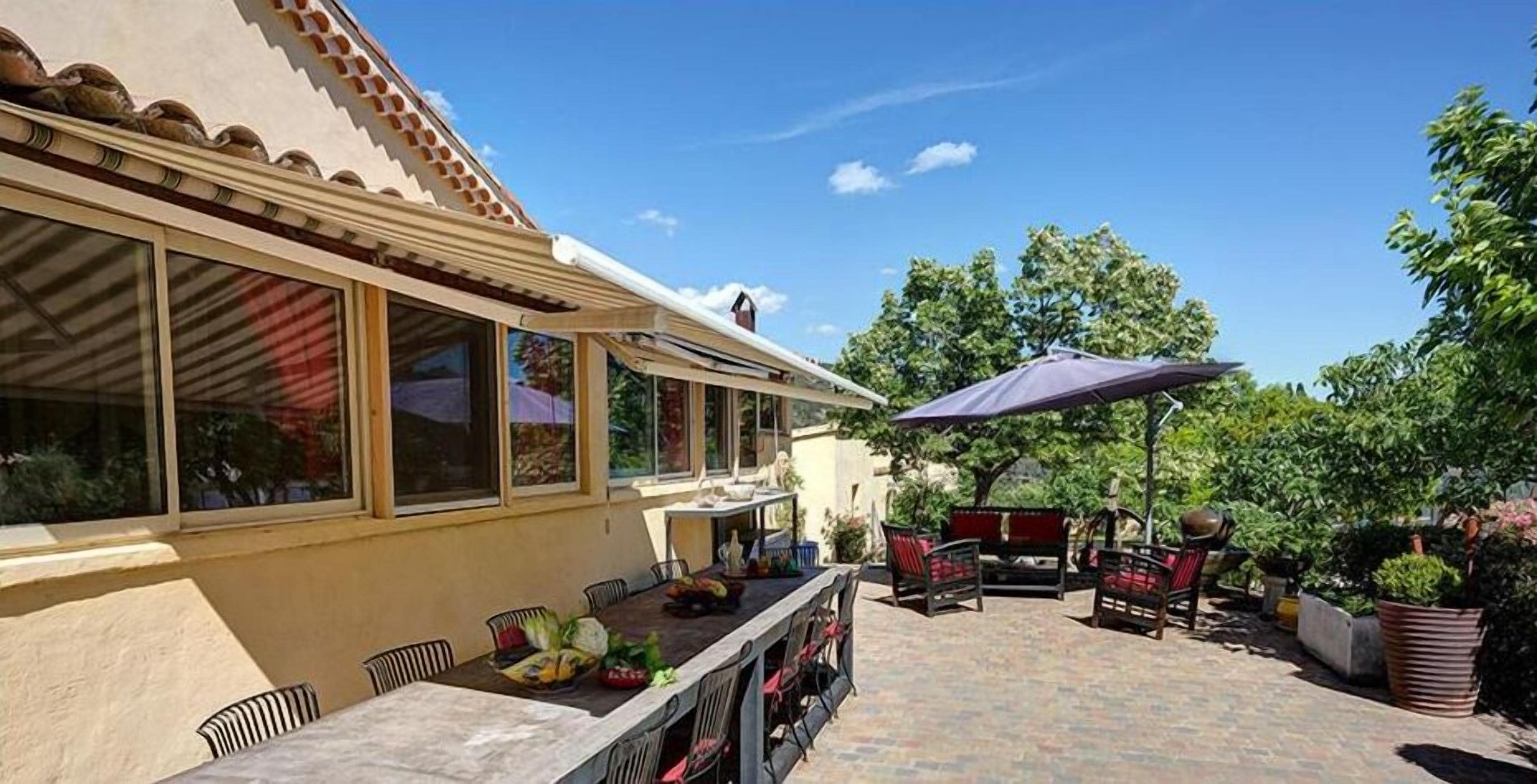 Eine Terrasse im Freien mit Esstisch, Stühlen und einem großen Sonnenschirm.