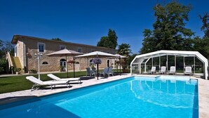 A swimming pool with lounge chairs and umbrellas, a covered seating area, and a stone building in the background. - Chateau Pontet d'Eyrans & Spa (Eyrans)