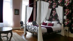 A four-poster canopy bed with white drapes, a floral wallpaper backdrop, and a small bedside table. - Chateau Pontet d'Eyrans & Spa (Eyrans)