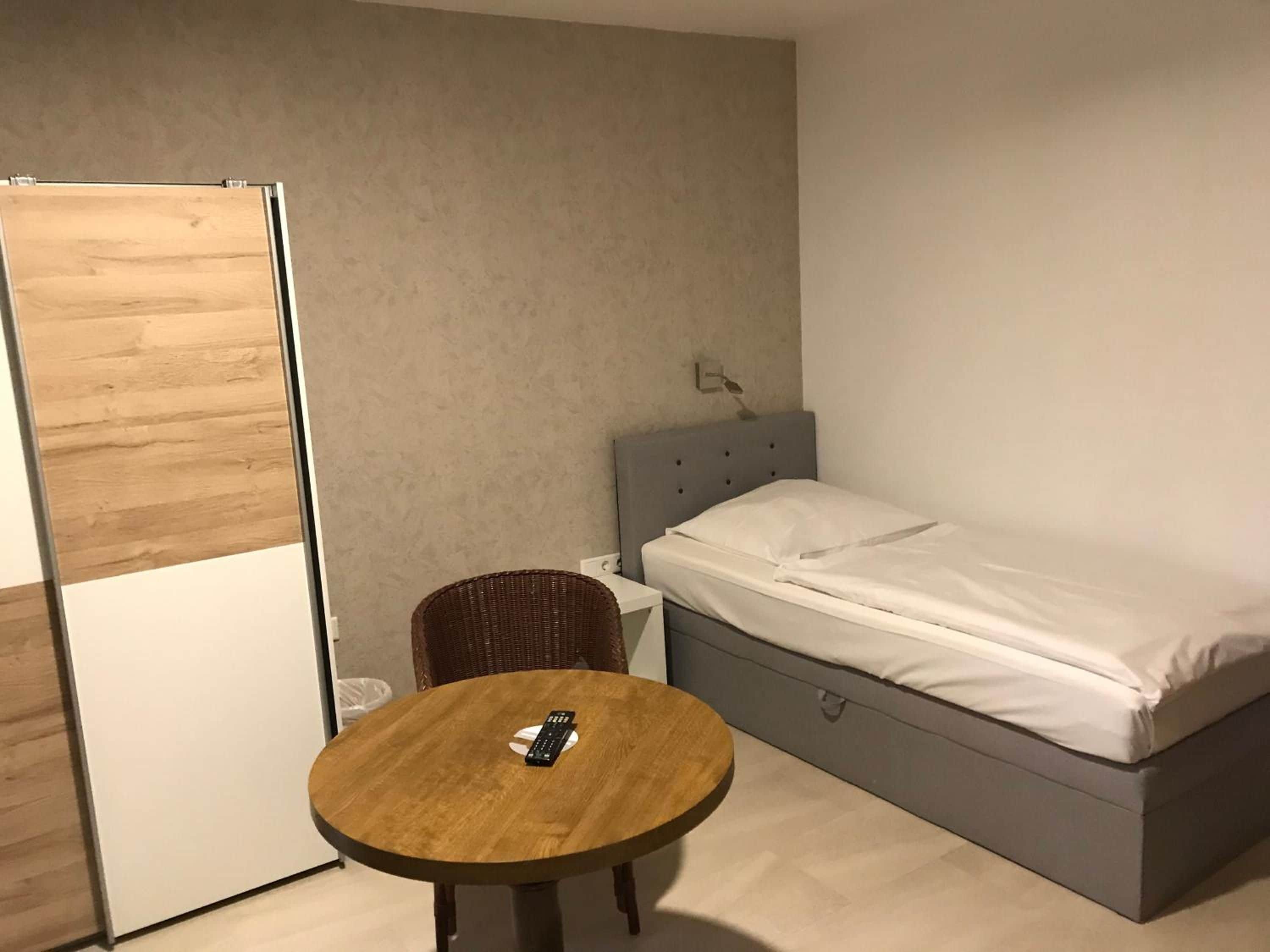 A bedroom with a bed, a bedside table, a chair, and a round table.