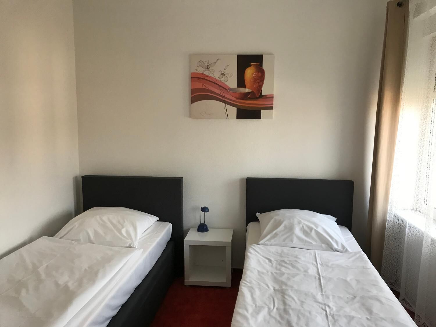 Una habitación de hotel con dos camas individuales, una mesita de noche pequeña con lámpara y un cuadro en la pared.