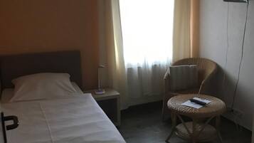 A hotel room with a bed, a bedside table with a lamp, a chair, and a flat-screen TV mounted on the wall.