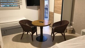 A room with a bed, a TV mounted on the wall, a small round table with two chairs, and a window with blinds. - Hotel Weinberg (Cremlingen)