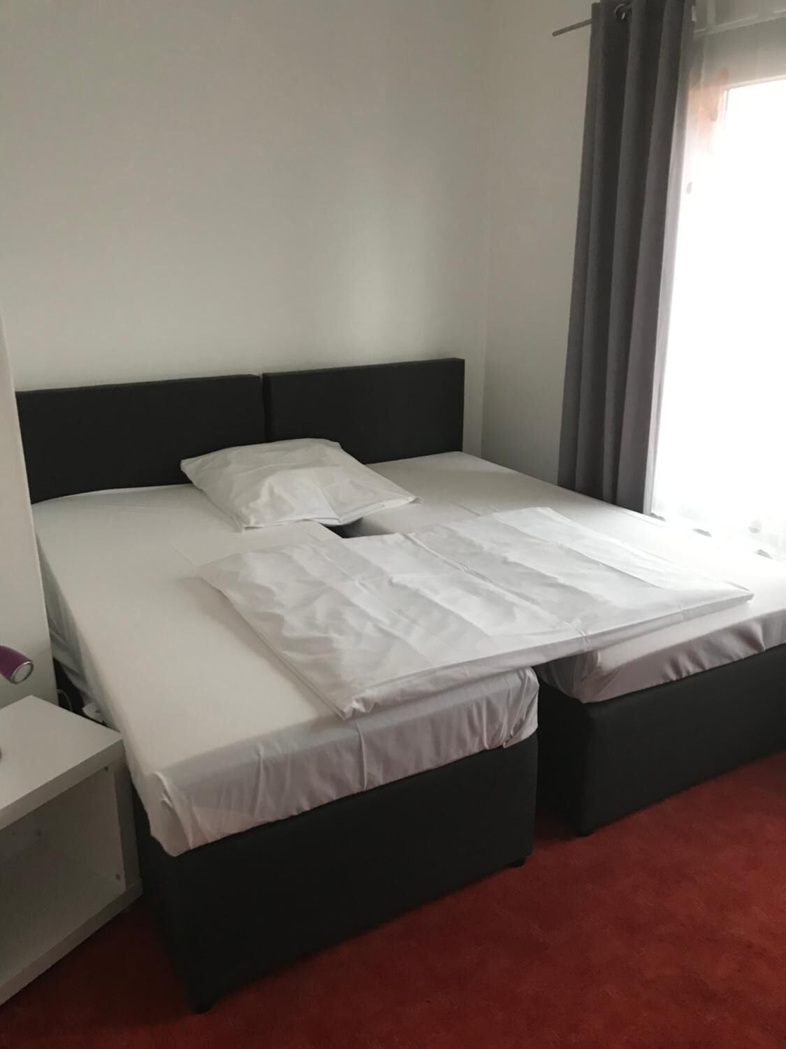 Una cama doble con cabecera negra, ropa de cama blanca y alfombra roja.