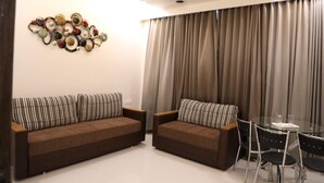 A modern living room with two brown sofas, a glass coffee table, and a ceiling fan. - Hotel Pushpak Park (Osmanabad)