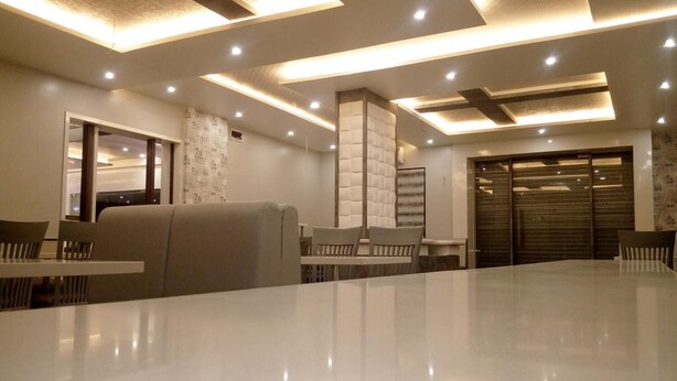A modern dining area with a long table and multiple chairs, recessed ceiling lighting, and a large window. - Hotel Pushpak Park (Osmanabad)