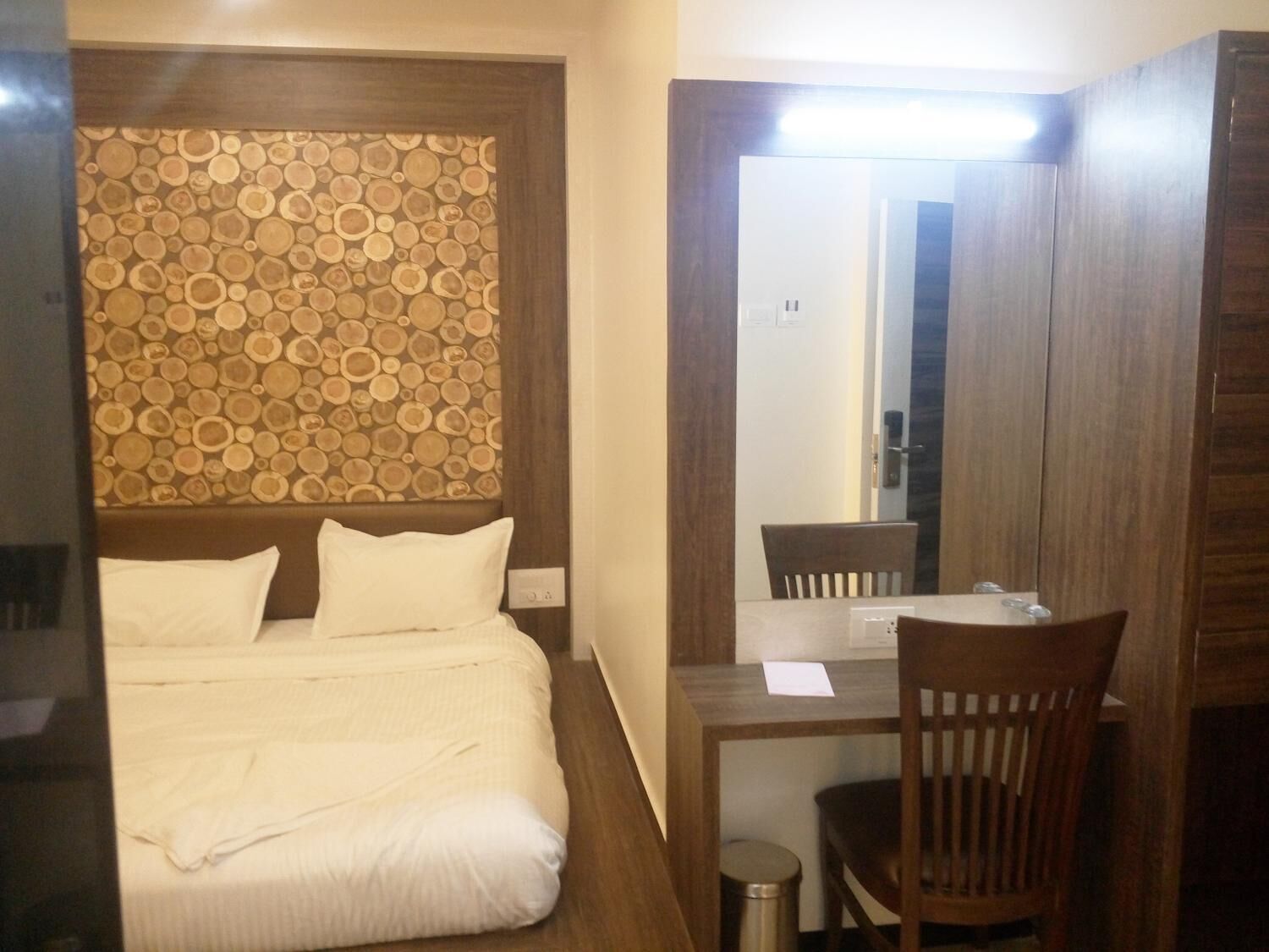 Een hotelkamer met een bed, een houten hoofdeinde, een bureau met een stoel en een spiegel.