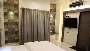 A hotel room with a bed, a shower area with curtains, a mounted TV, and an air conditioning unit. - Hotel Pushpak Park (Osmanabad)