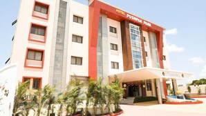 A multi-story hotel with a prominent red and white facade, a covered entrance, and a landscaped front garden. - Hotel Pushpak Park (Osmanabad)