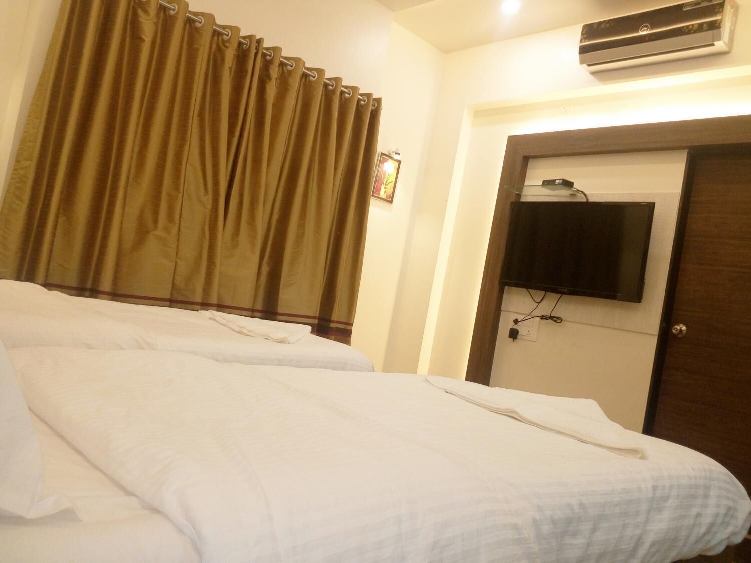 Une chambre d’hôtel avec deux lits, un téléviseur fixé au mur et un appareil de climatisation placé au-dessus de la porte.