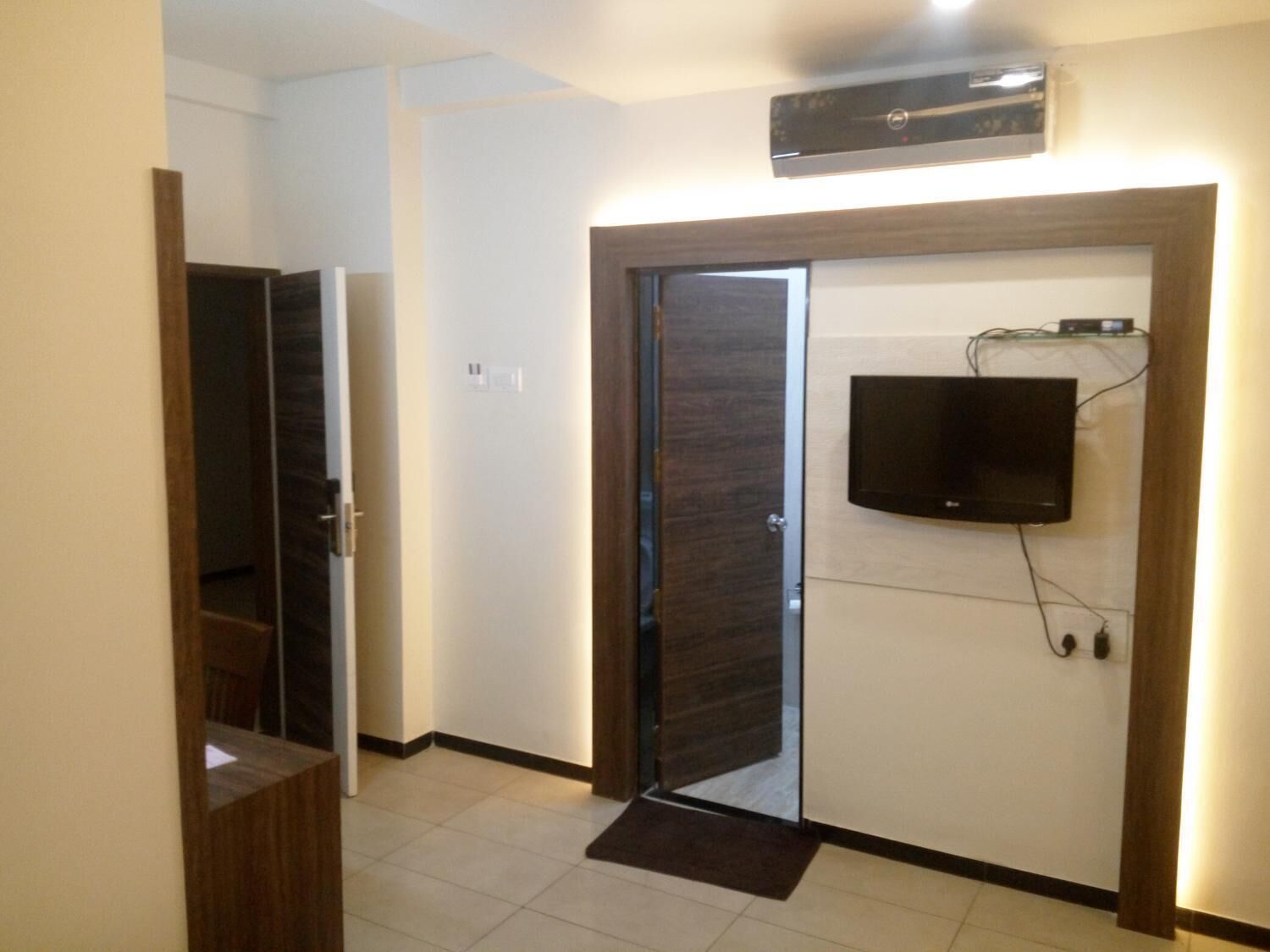 A hallway with a wooden door, a small step leading to a room, and a mounted television on the wall.
