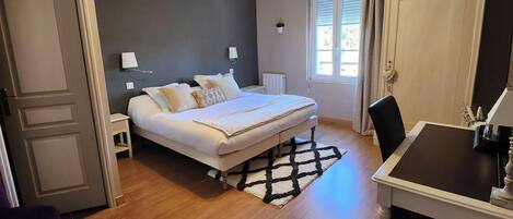 Un dormitorio con cama, mesitas de noche, ventilador de techo, ventana con cortinas y suelo de madera.
