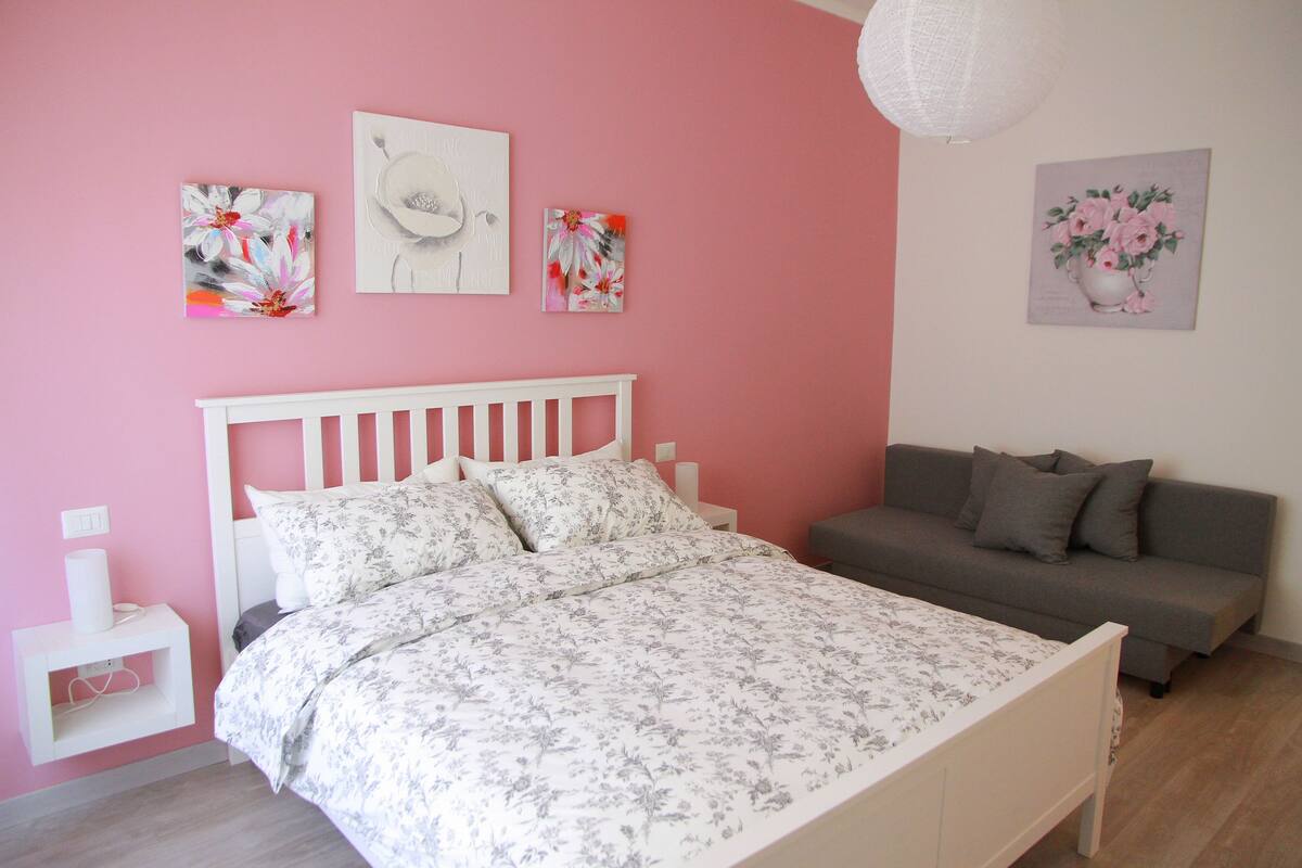 Un dormitorio con una cama blanca, un sofá gris y paredes rosas.
