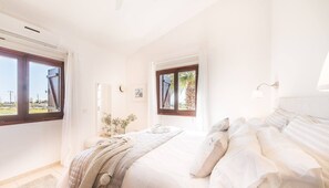 Un dormitorio con una cama grande, dos ventanas, una mesita de noche y un buró.