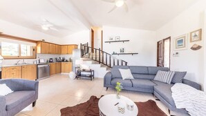 A modern living room with a grey sofa, a coffee table, and a kitchen area with wooden cabinets and a built-in oven. - Villa Isabella (Pegeia)