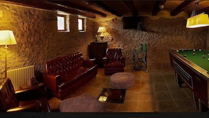 Una habitación acogedora con mesa de billar, sofá de cuero y paredes de piedra.