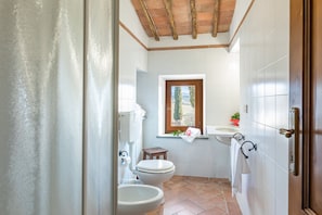 Une salle de bain comprenant des toilettes, un bidet, un lavabo et une fenêtre donnant sur des arbres.