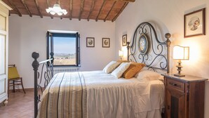 Een slaapkamer met een bed, nachtkastje, raam en uitzicht op het platteland.