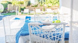 A poolside area with white wicker chairs and a table with a blue-striped tablecloth. - Villa Jaimi (Pegeia)