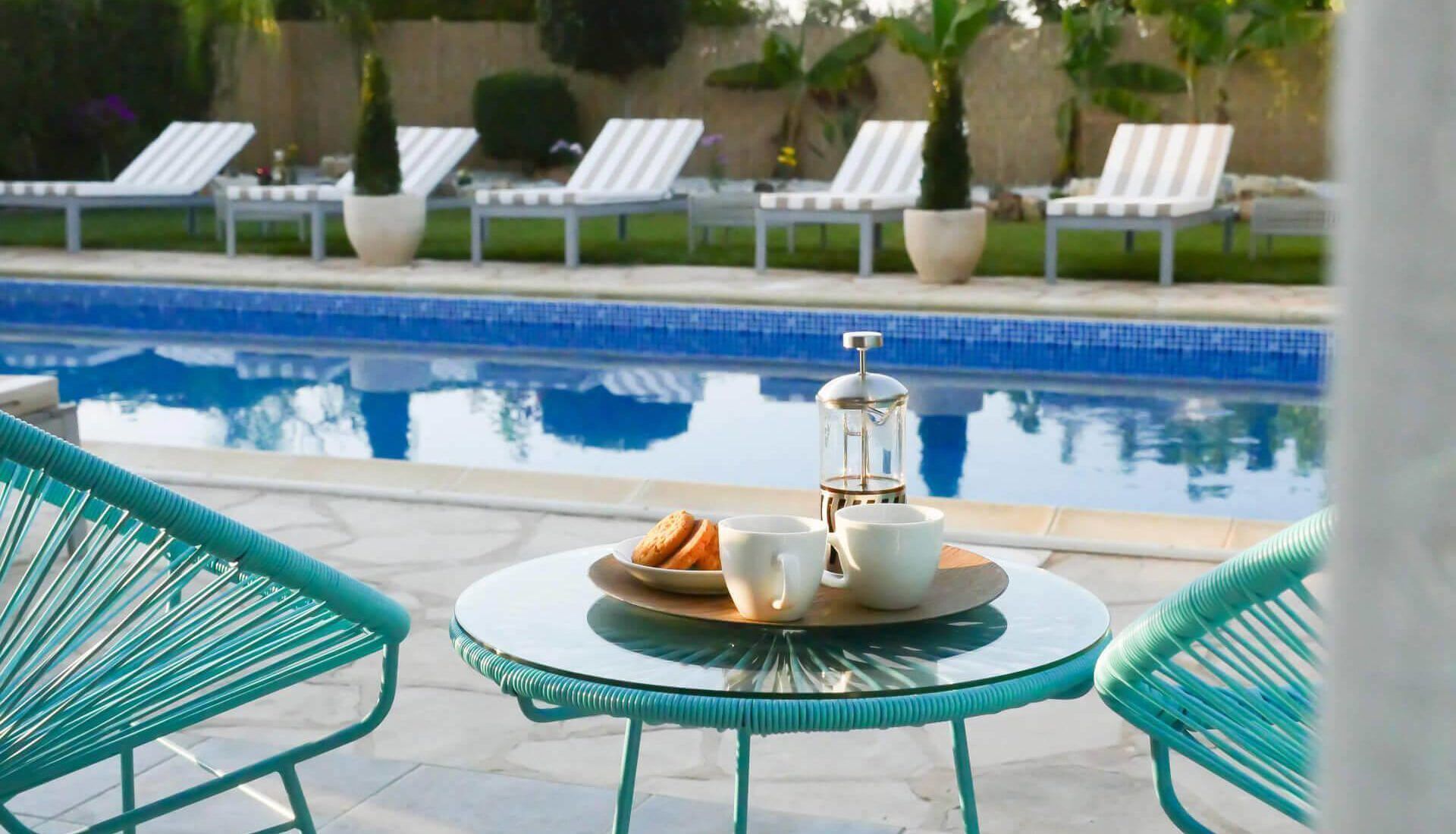 Un espace aménagé au bord de la piscine, avec une table dressée pour deux personnes, une cafetière et une assiette de biscuits.