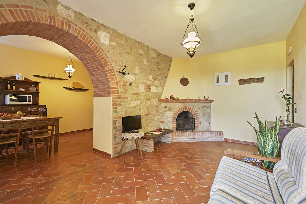 A living room with a brick fireplace, a television on a stand, a dining table with chairs, and a sofa.