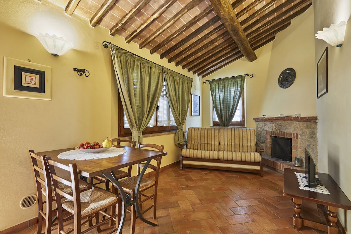 A dining area with a wooden table and chairs, a sofa, and a fireplace.