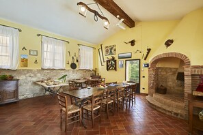 Un comedor con una gran mesa de madera y sillas, chimenea de ladrillo y pared de piedra.