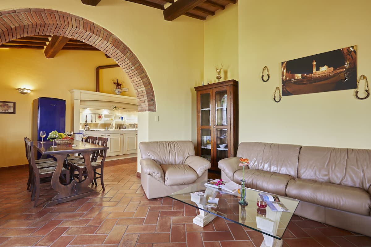 A living room with a dining table, two sofas, a glass coffee table, and a kitchen in the background.