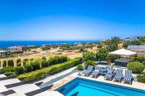 A pool area with lounge chairs and a view of the sea.