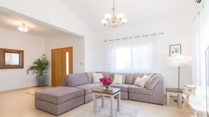 Una sala de estar con un sofá modular, una mesa de centro, una planta en maceta y una araña.
