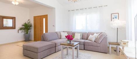 A living room with a sectional sofa, a coffee table, a potted plant, and a chandelier.