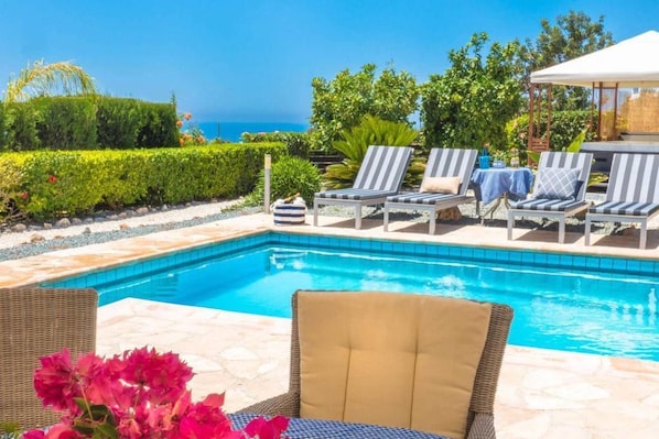 A poolside area with lounge chairs, a wicker chair, and a table with a checkered tablecloth.