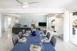 Un comedor con mantel azul, platos blancos y un jarrón azul. Hay un sofá y un televisor al fondo.