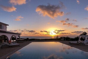 An infinity pool with a sunset view, lounge chairs, and a building with arches. - Villa Searay (Paphos)