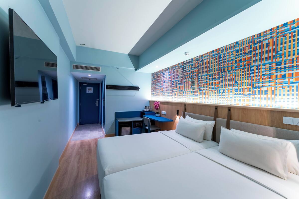 Una habitación de hotel moderna con una cama grande, un escritorio y una llamativa obra de arte abstracta en la pared.