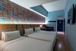 Quarto de hotel com duas camas, uma escrivaninha e uma grande obra de arte na parede.
