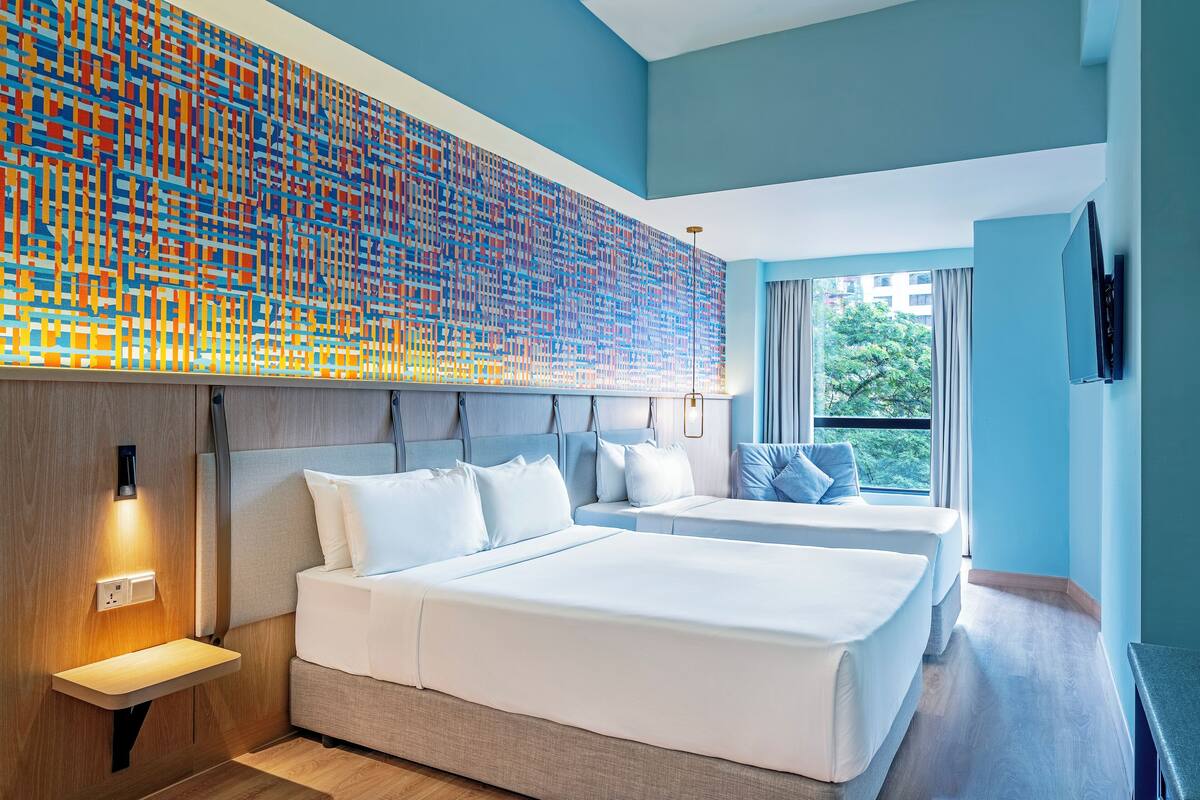 Una habitación de hotel moderna con una cama grande, una cama más pequeña, una mesita de noche, una obra de arte en la pared y una ventana con vistas a zonas verdes.