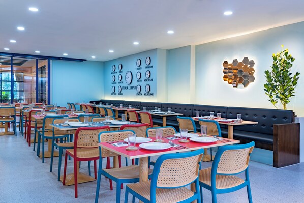 Un restaurante con varias mesas y sillas, una pared con relojes que marcan diferentes ciudades y un adorno de pared.