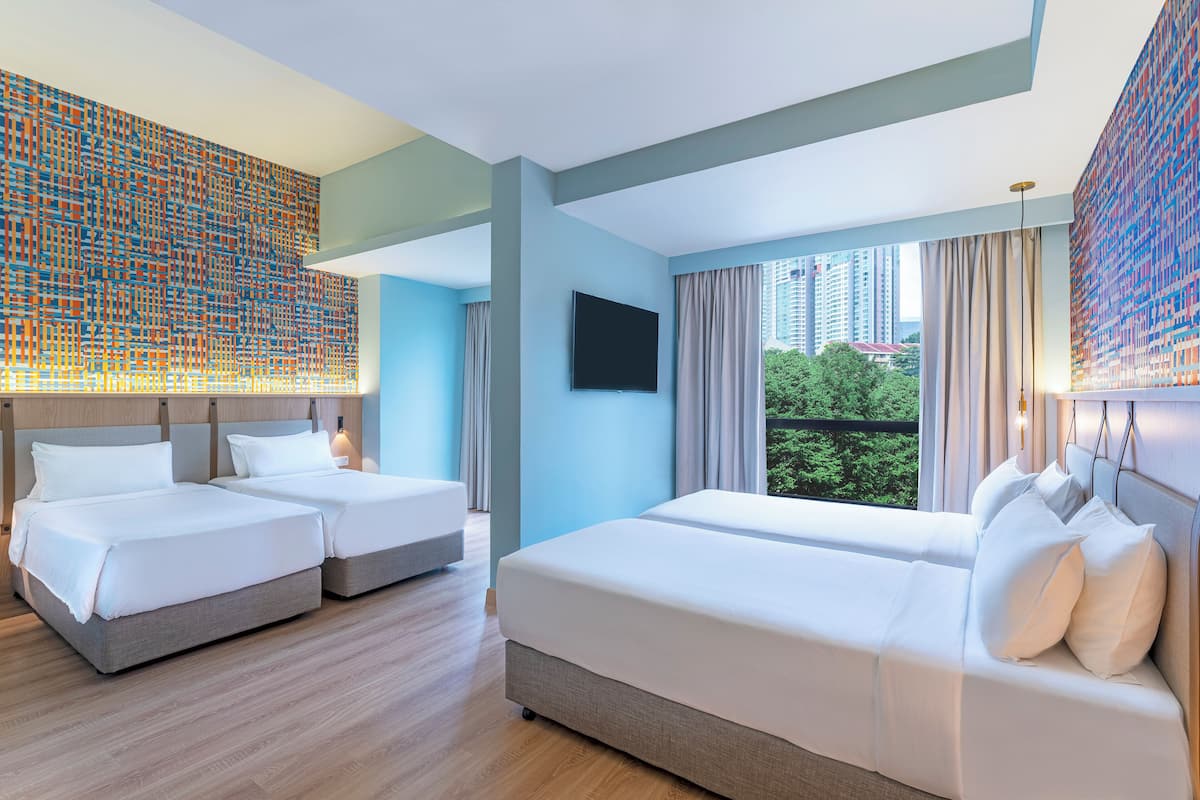 Una habitación de hotel con dos camas, un ventanal con vistas a edificios y una pared con un motivo colorido.