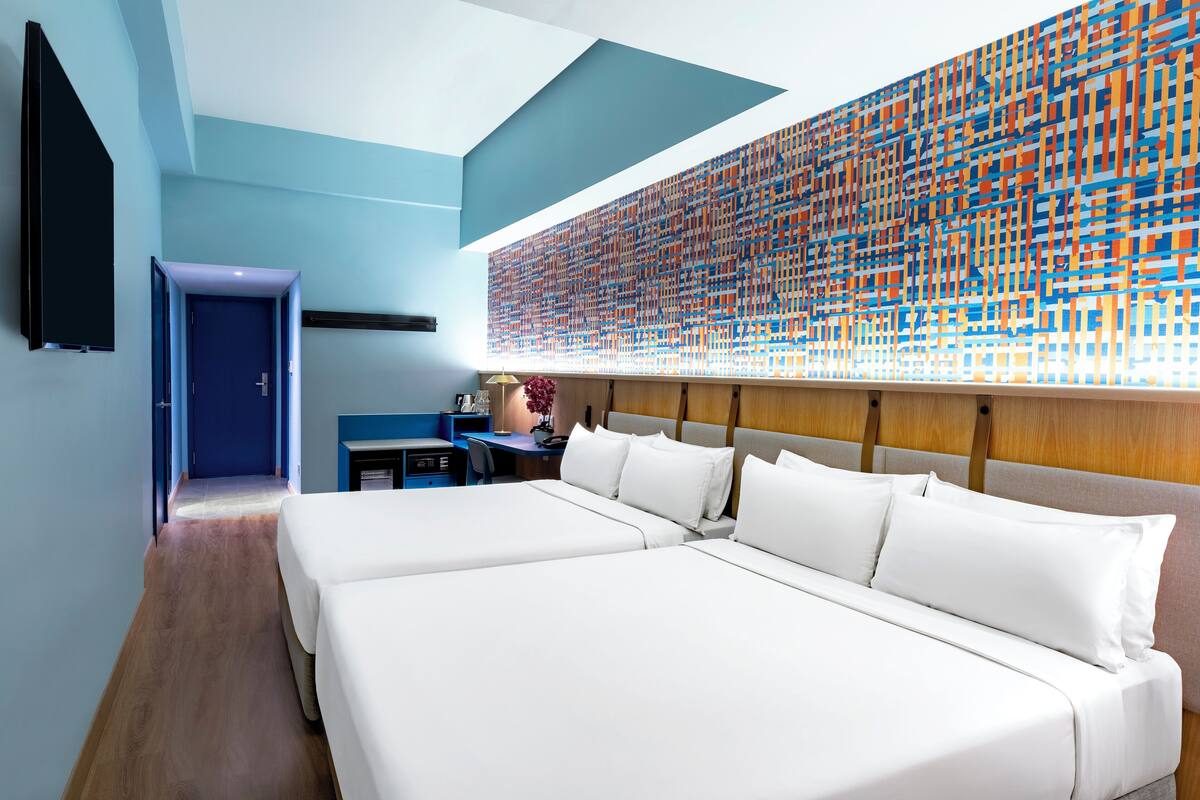 Habitación de hotel con dos camas, un escritorio y un cuadro abstracto grande en la pared.