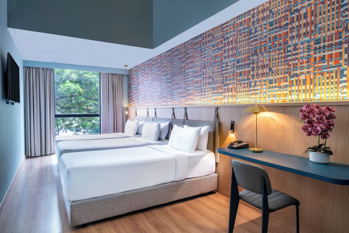 Una habitación de hotel moderna con una cama grande, un escritorio y vistas a zonas verdes por la ventana.
