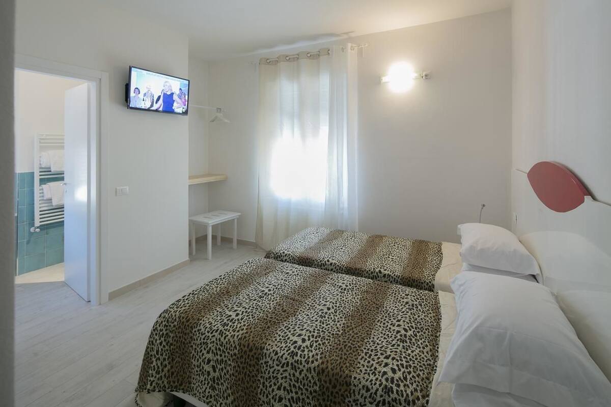 Un dormitorio con dos camas, un televisor en la pared, una mesita pequeña y una ventana con cortinas.
