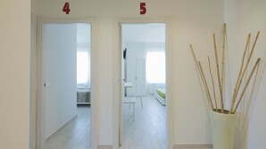 Een gang met deuren met de nummers 4 en 5 die leiden naar een kamer met een bed en een bankje. Rechts is een bamboestokarrangement zichtbaar.