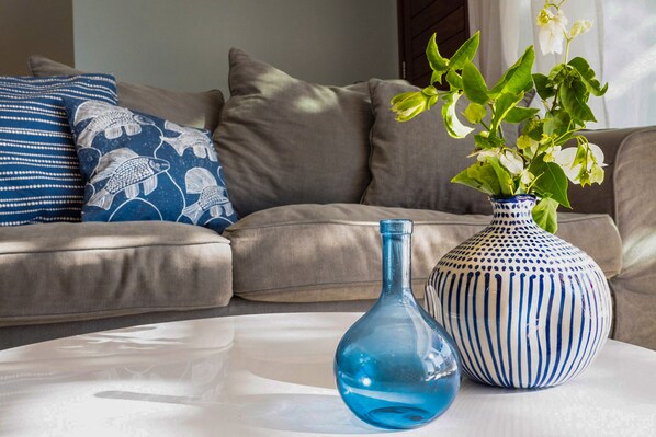 Un salon avec un canapé beige, un vase bleu contenant des plantes vertes et une bouteille en verre bleue posée sur une table blanche.