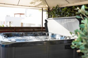 A hot tub with a metal frame and a white cover, surrounded by greenery and a wooden deck.